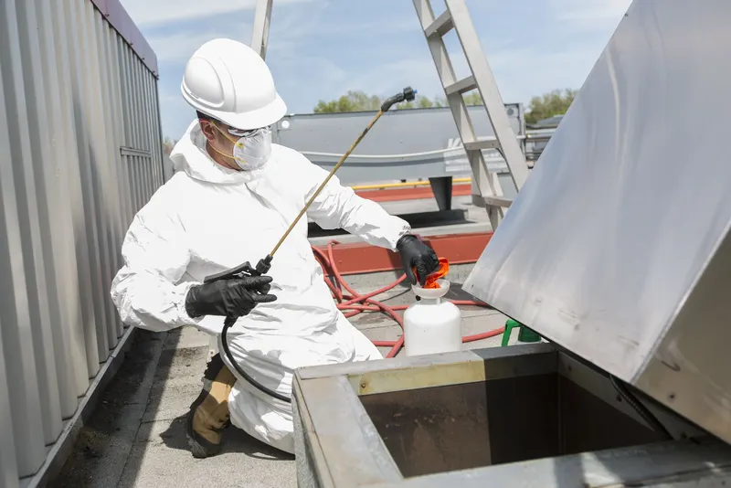 Rooftop kitchen exhaust fan tipped open on its hinge above a commercial building roof, with the wheel and housing exposed