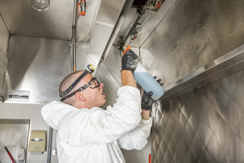 Degreaser being sprayed under the edge of a stainless hood canopy, the same method used on a food truck hood