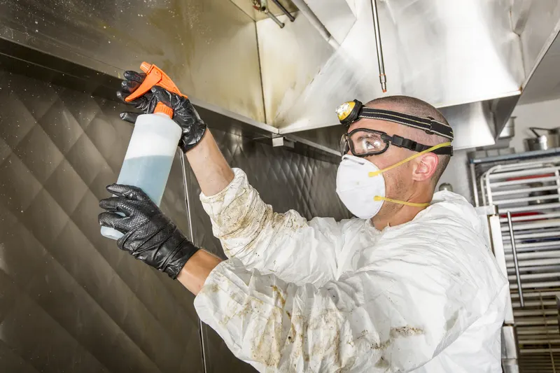 Spray bottle of degreaser held beside a stainless steel kitchen exhaust canopy before cleaning begins